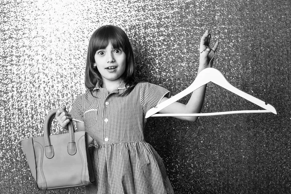 Pequeña chica bastante sorprendida con bolsa de cuero rojo y percha — Foto de Stock