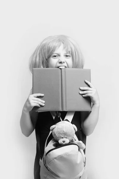 Девушка с рюкзаком и игрушками кусает большую синюю книгу — стоковое фото