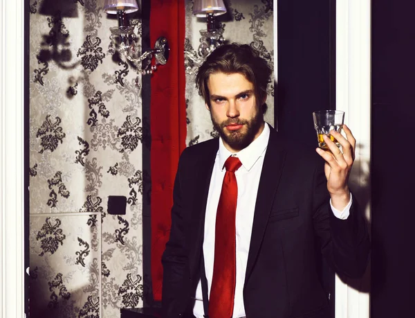 Brodaty mężczyzna, biznesmen w garniturze, czerwony krawat trzyma szklankę whisky — Zdjęcie stockowe