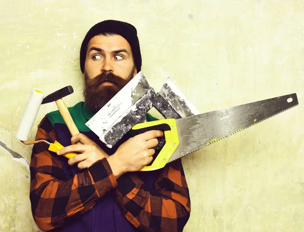 Бородатий чоловік тримає різні будівельні інструменти з здивованим обличчям — стокове фото