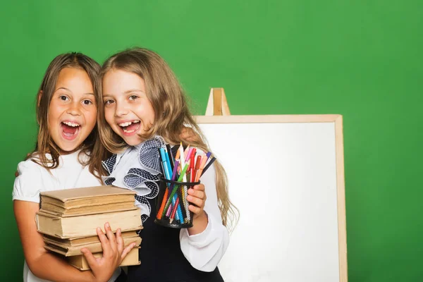 Schoolgirls with happy faces hug. Children hold pile of books — Stock Photo, Image