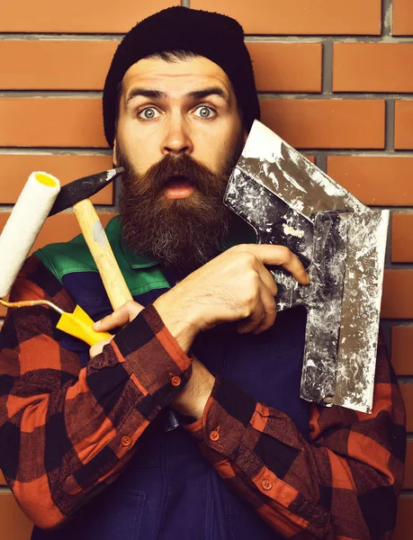 Бородатый мастер держит различные строительные инструменты с удивленным па — стоковое фото