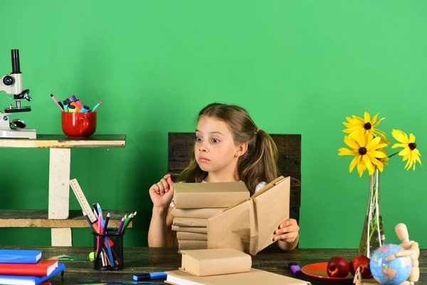 Kız şok yüzü ile ders kitabı tutar. Çocuk ve okul malzemeleri