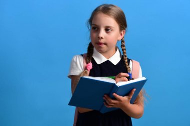 Kız büyük mavi bir defterle yazıyor. Okul üniformalı bir öğrenci.