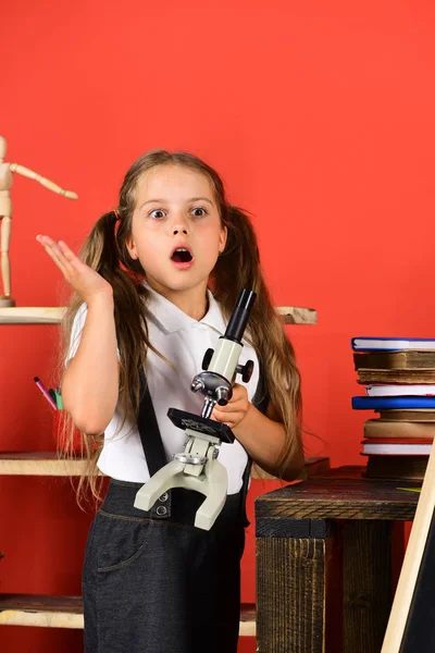 Schoolgirl with shocked face near bookshelf with school items — Stock Photo, Image