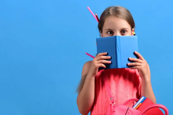 Chica con el bolso de la escuela se esconde detrás del cuaderno azul —  Fotos de Stock