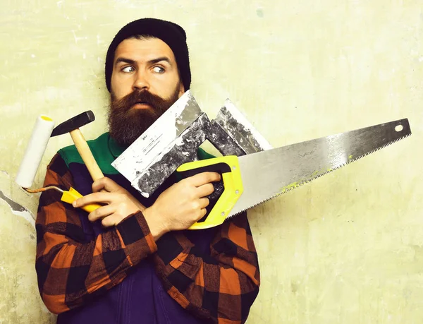 Бородатый человек держит различные строительные инструменты с удивленным лицом — стоковое фото