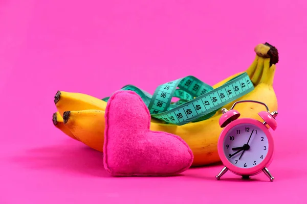 Sammansättningen av väckarklocka, hjärta och måttband på bananer — Stockfoto
