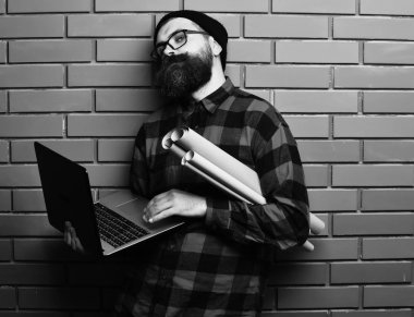 Kaba sakallı, beyaz tenli hippi elinde dizüstü bilgisayar ve el işi kâğıdı tutuyor.