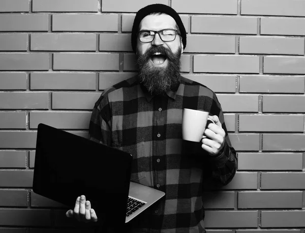 Skäggig brutal kaukasisk hipster som håller laptop med kopp — Stockfoto