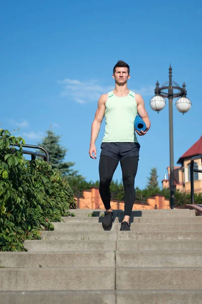 Mannen idrottsman i träningsoverall med gym yogamatta kommer trappa ner — Stockfoto