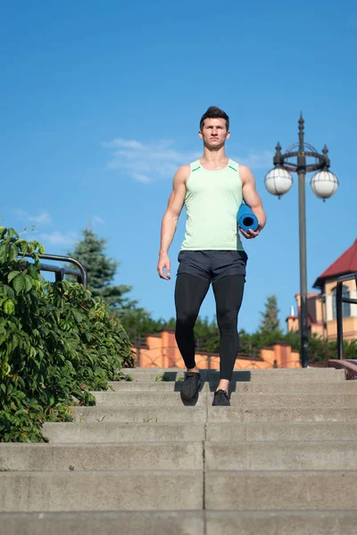 Hombre atleta en chándal con colchoneta de yoga gimnasio va abajo —  Fotos de Stock