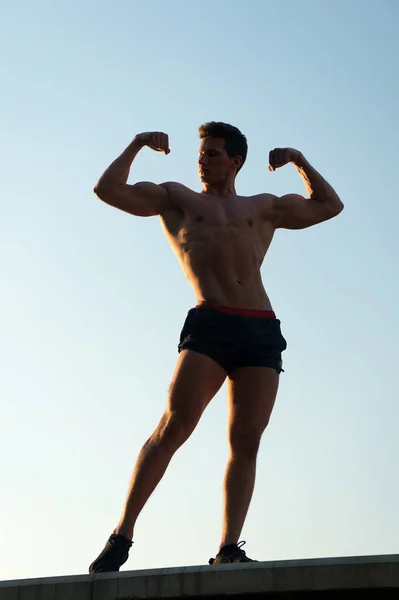 ผู้ชายที่แสดงร่างกายที่เหมาะสมบนท้องฟ้าสีฟ้า — ภาพถ่ายสต็อก