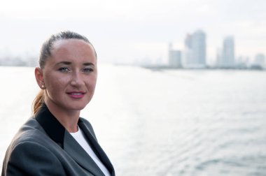 Yüzü çilli, ceketli, denizde poz veren bir iş kadını.