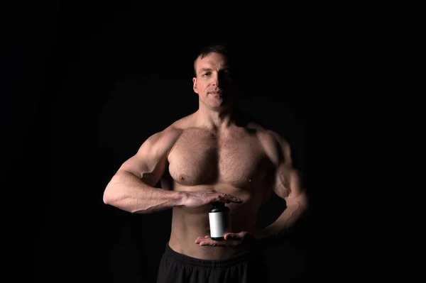 Человек с мускулистым телом держать банку с таблетками, спорт . — стоковое фото