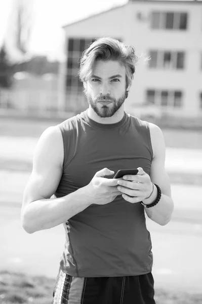 Homme barbu athlétique avec corps musculaire tient téléphone cellulaire — Photo