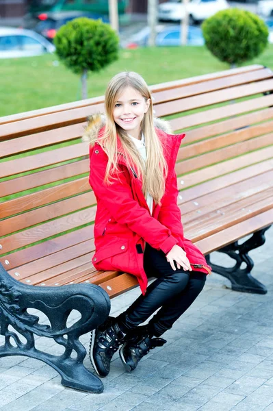 Dziewczyna w czerwonym płaszczu siedzieć na ławce w parku — Zdjęcie stockowe