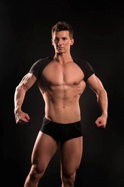 Мужчина спортсмен показывает мускулистое тело на темном фоне — стоковое фото