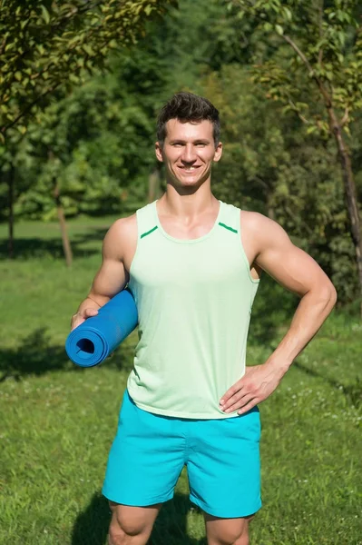 Sportowiec uśmiech z matę do jogi niebieski w ręce w parku — Zdjęcie stockowe