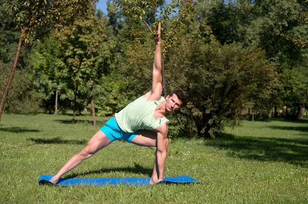 Atleta allungare le mani e le gambe sul tappeto blu nel parco — Foto Stock