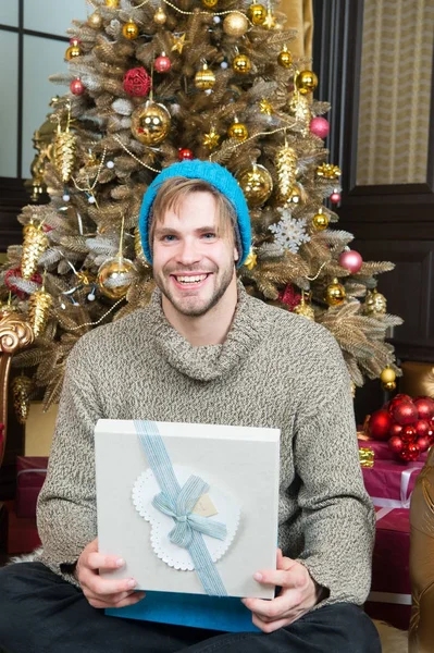 Χαμόγελο ο άνθρωπος με το καπέλο, πουλόβερ με παρόν στο χριστουγεννιάτικο δέντρο — Φωτογραφία Αρχείου