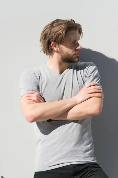 Muž v tričku póza se založenýma rukama na šedé stěně — Stock fotografie