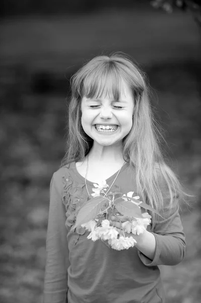 Niña pequeña con la cara sonriente sosteniendo flor de sakura rosa — Foto de Stock