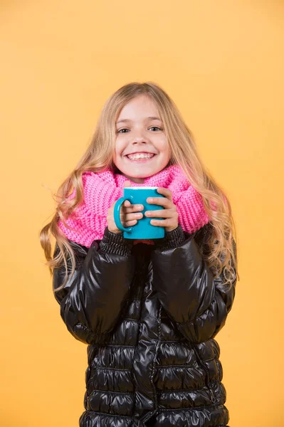 Child hold mug in black jacket and pink scarf