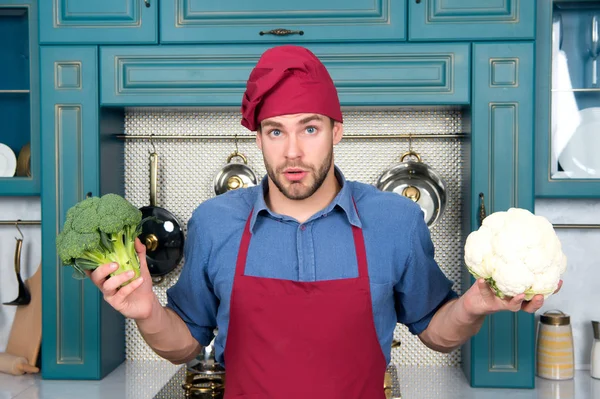 Macho-Koch mit überraschtem Gesicht hält Blumenkohl und Brokkoli in der Hand — Stockfoto