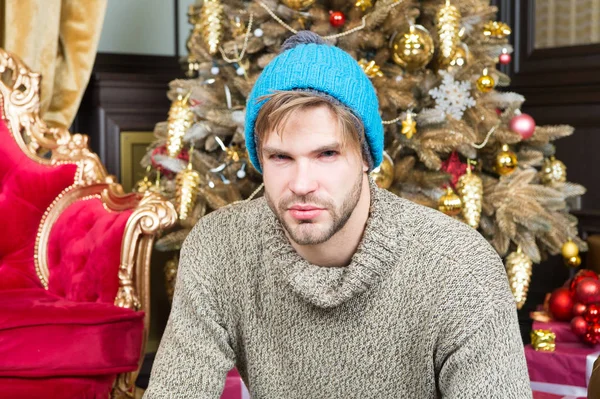 Macho en sombrero caliente, suéter sentarse en el árbol de Navidad — Foto de Stock