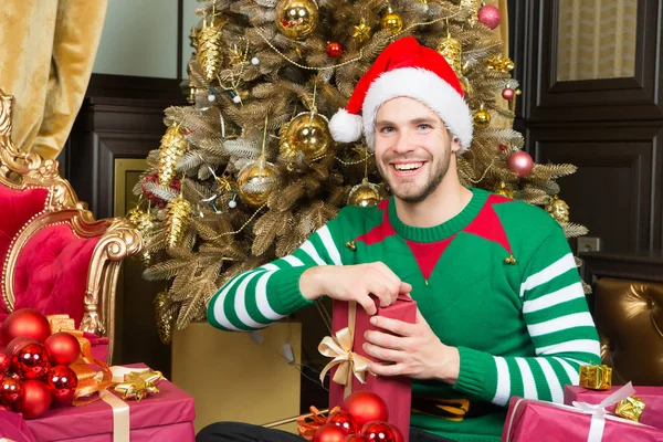 Hombre en la sonrisa del sombrero de santa con regalos en el árbol de Navidad — Foto de Stock