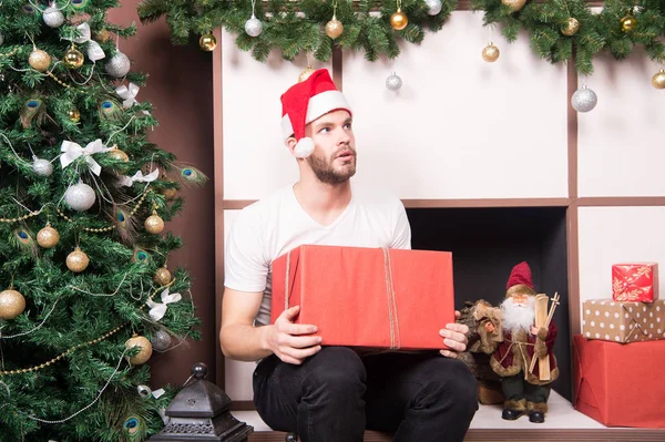Guy with serious face in santa hat hold present box — Stock Photo, Image
