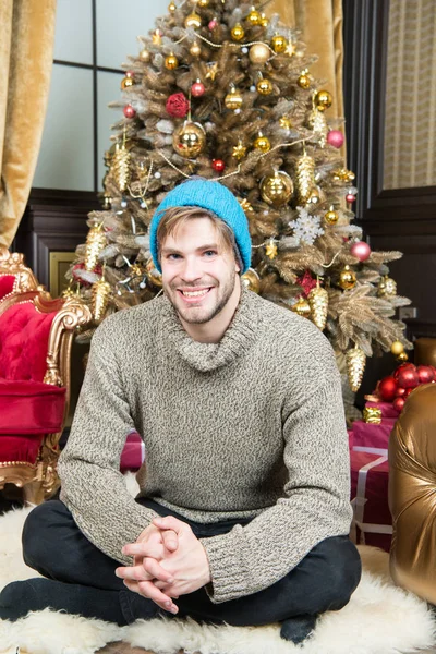 Ο άνθρωπος χαμόγελο σε ζεστό καπέλο, πουλόβερ στο χριστουγεννιάτικο δέντρο — Φωτογραφία Αρχείου