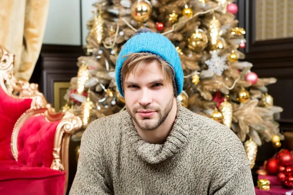 Ο τύπος σε ζεστό καπέλο, να καθίσει πουλόβερ στο χριστουγεννιάτικο δέντρο — Φωτογραφία Αρχείου