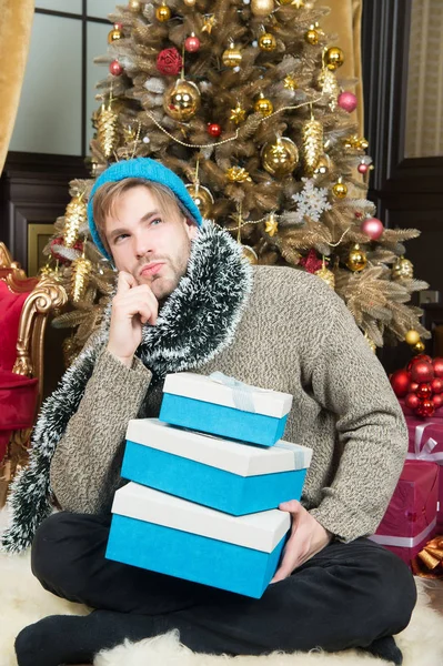 Hombre con cara de pensar en sombrero, suéter sujetar regalos envueltos — Foto de Stock