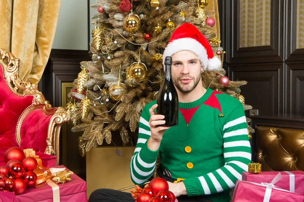 Man in kerstmuts met een champagnefles bij kerstboom — Stockfoto