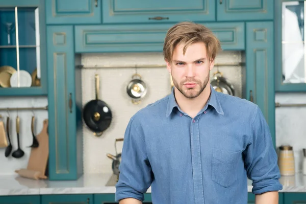 Чоловік з серйозним обличчям у синій сорочці стоїть на кухні — стокове фото
