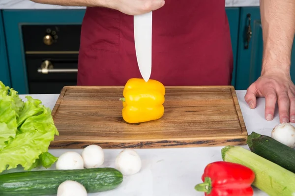 Рука вирізає жовтий перець з ножем на дерев'яній обробній дошці — стокове фото