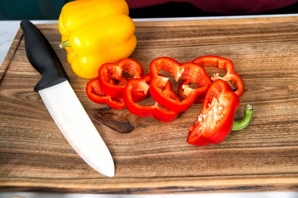 Перець нарізає овочевий та керамічний ніж на дерев'яній обробній дошці — стокове фото