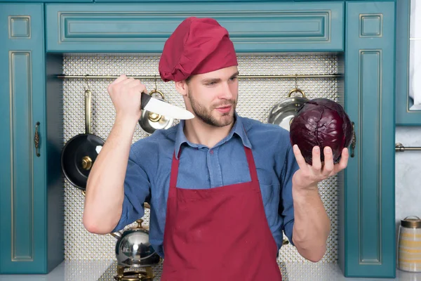 Чоловік шеф-кухар в червоній шапці тримає фіолетову капусту і ніж — стокове фото