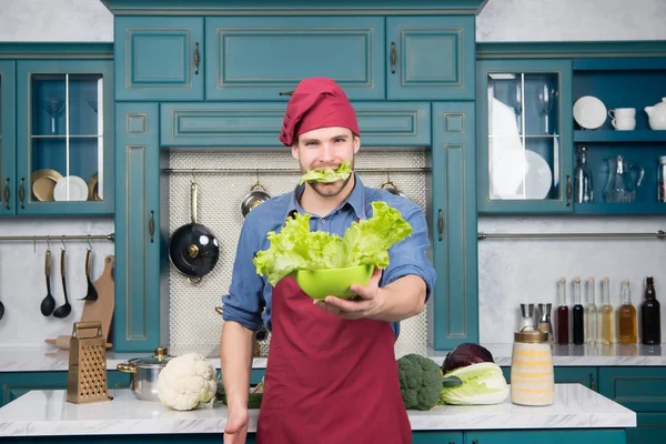 Macho houd groene blad in mond en salade in kom — Stockfoto