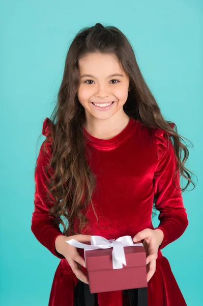 Šťastné dítě v červených šatech drží box na modrém pozadí — Stock fotografie