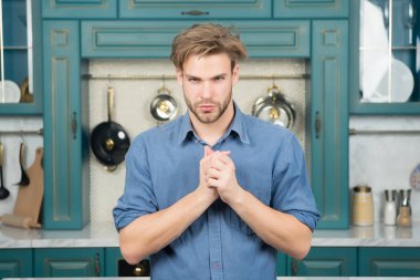 Maço ile ciddi bir yüz, sarı saçlı mavi gömlekli hazır mutfak katlanmış parmak ile. Yiyecek hazırlama, kavram yemek mutfağı.