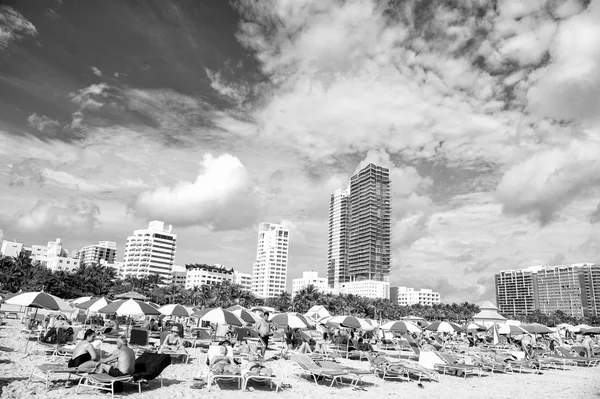 マイアミ アメリカ合衆国 2016 マイアミビーチやサウスビーチ 人曇りの青空に高層ビルとビーチに青い傘の下でデッキチェアで日光浴します 夏休み ラウンジとレジャー — ストック写真