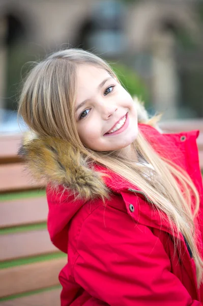 Дівчина в червоному пальто сидить на лавці в парку — стокове фото