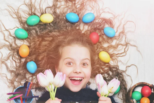 Feliz chica de Pascua, huevos de colores en el pelo largo, flores de tulipán — Foto de Stock