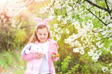 Bahçede çiçek açan ağaçlarla tavşan kulaklarıyla gülümseyen bir çocuk.