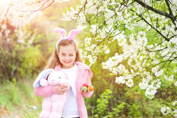 Bahçede çiçek açan ağaçlarla tavşan kulaklarıyla gülümseyen bir çocuk.