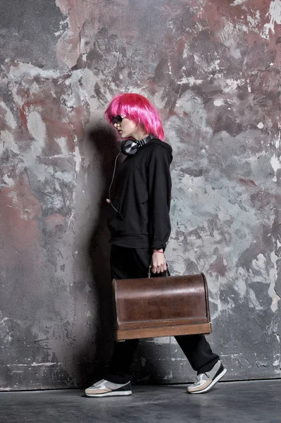 Mujer en peluca de pelo rosa, auriculares llevan maleta retro — Foto de Stock