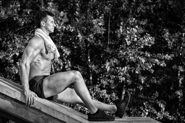 Человек с мускулистым телом и игрушкой, сидящий на бетонном серфе — стоковое фото
